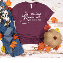 Load image into Gallery viewer, a t - shirt with the words amazing grace on it next to a pile of
